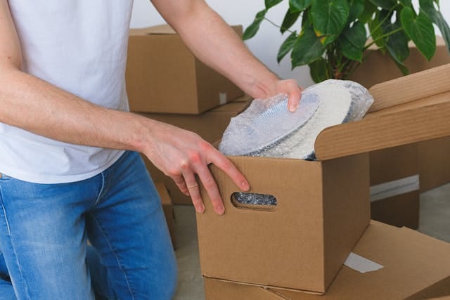 A person packing dishes into a cardboard box