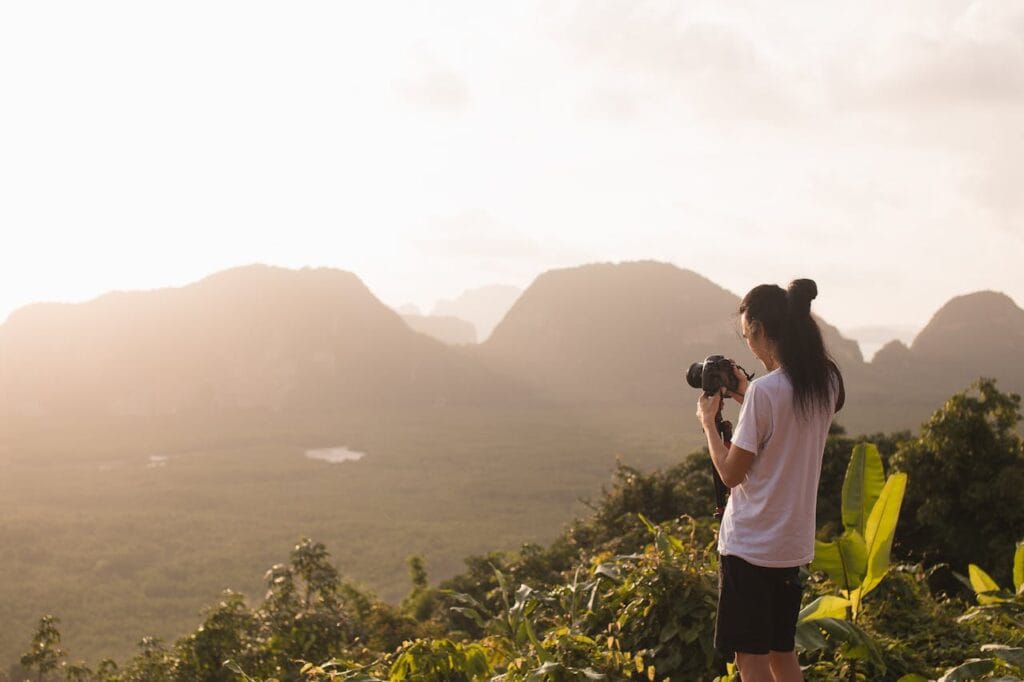 A photographer standing on a hilltop, photographing a misty mountain landscape at golden hour.